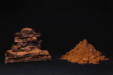 Close up view of dry cocoa powder near chocolate on black background 