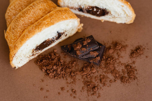Top view of chocolate and dry cocoa near croissant on brown background 
