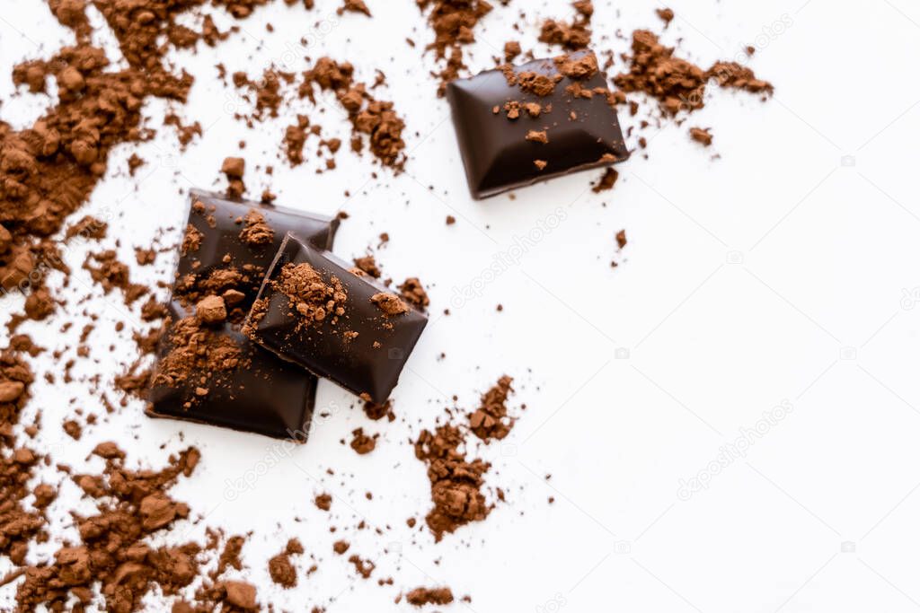 Top view of blurred cocoa powder on chocolate pieces on white background 