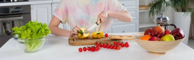 cropped view of woman cutting bell pepper near cherry tomatoes, lettuce and fresh fruits, banner