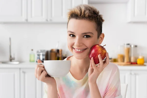 Happy Pangender Person Cup Tea Fresh Apple Looking Camera Kitchen — Foto Stock