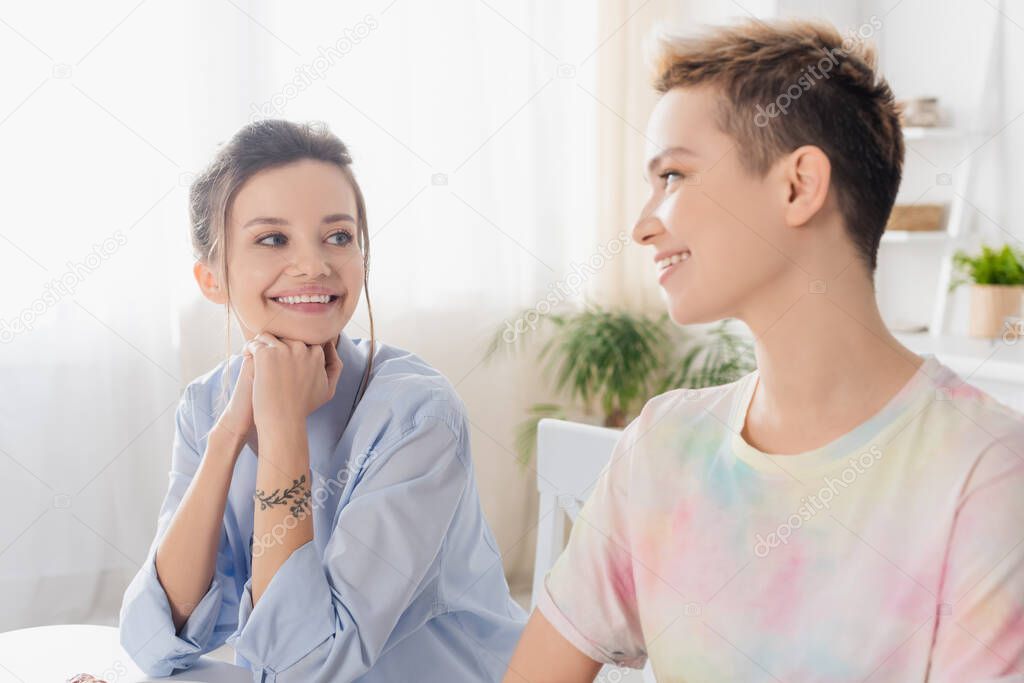 happy pangender couple smiling at each in kitchen