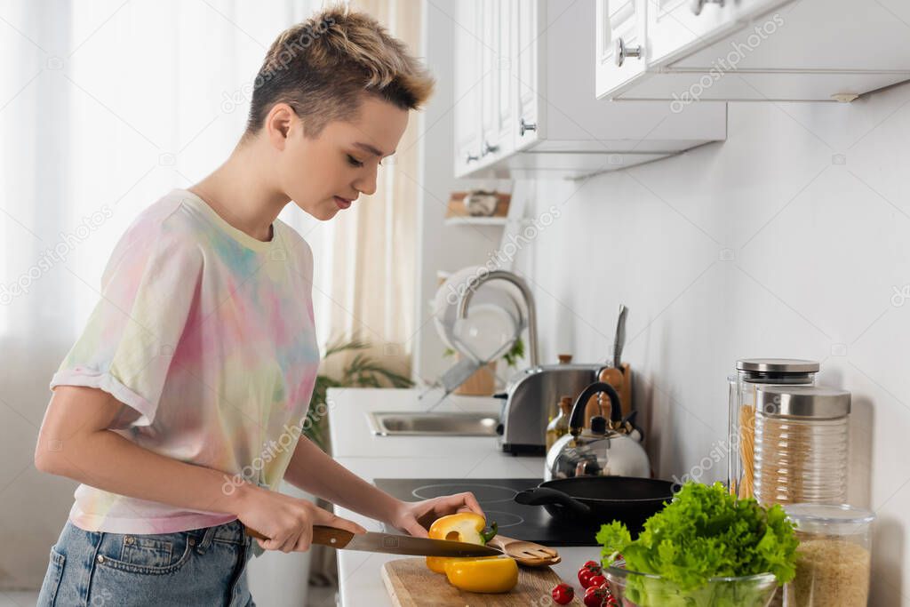 side view of pansexual person preparing breakfast and cutting bell pepper in kitchen