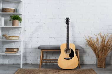 Akustik gitar, dikenli vazo, çivili vazo ve beyaz tuğla duvarın yanında sepet sepetleri.
