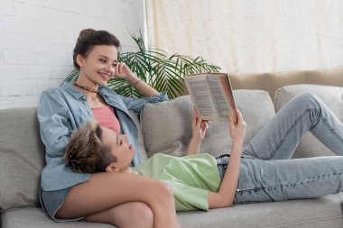 Panseksüel insan kanepede kitap okuyor. Gülümseyen partner yanında.