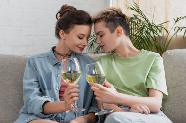 happy bigender couple sitting with closed eyes and wine glasses at home