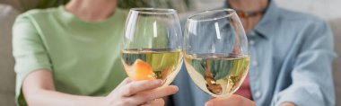 partial view of blurred pangender couple clinking glasses with white wine, banner
