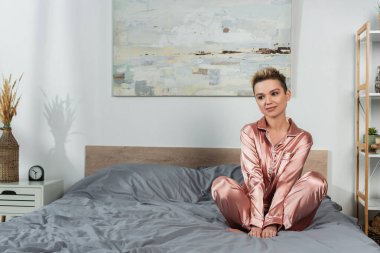 İpek pijamalarıyla yatakta oturan genç ve hayalperest bir kadın.