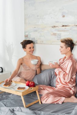 young pansexual lovers looking at each other during breakfast in bedroom