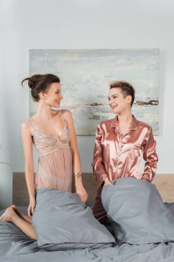 joyful pansexual lovers holding pillows and smiling at each other in bedroom