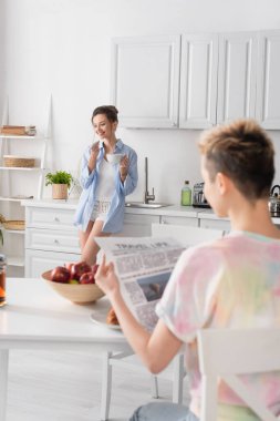 Bulanık panseksüel insan gazete okuyor. Yanında mutlu bir eş, bir fincan çayla.