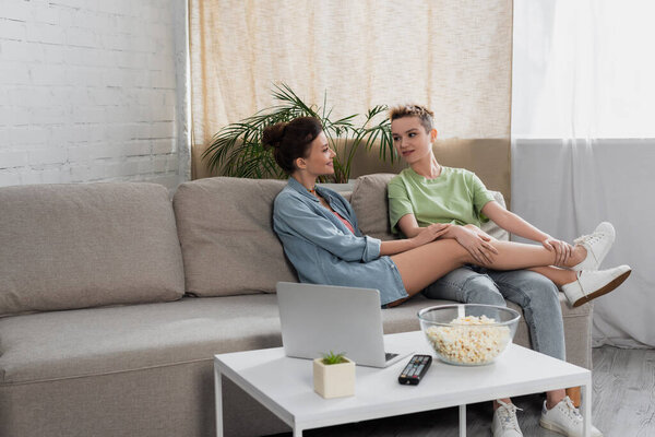 positive pansexual people talking on couch near laptop and bowl of popcorn