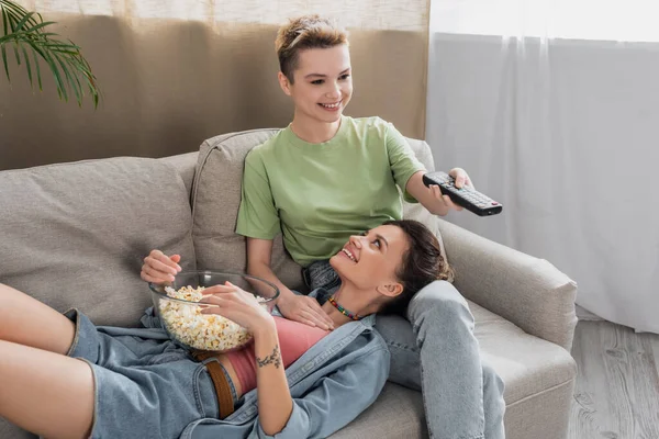 快乐的泛性别人士在沙发上与爆米花一起点击电视频道 — 图库照片