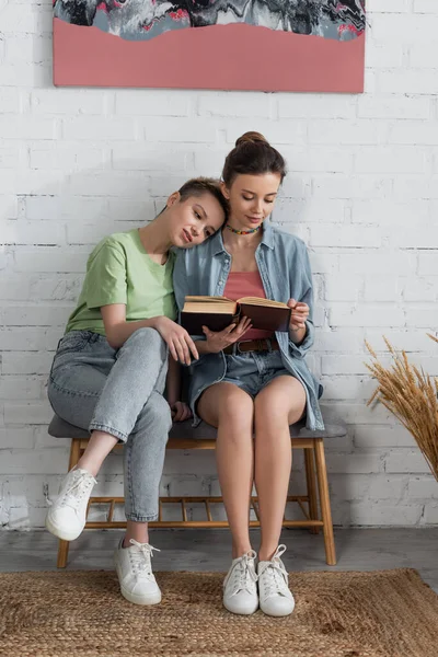 Full Length Young Pansexual Couple Sitting Ottoman Reading Book - Stock-foto