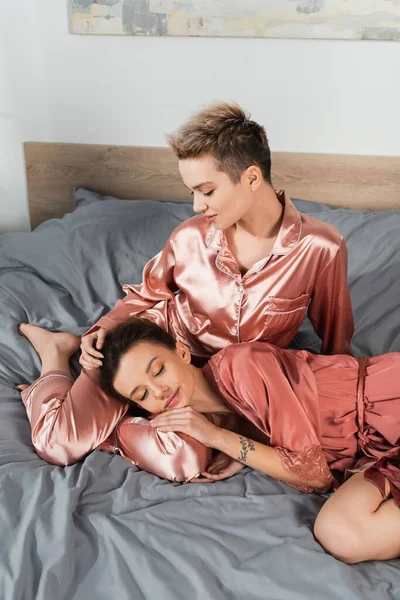 pansexual person sleeping near lover sitting on bed in silk pajamas