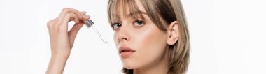 young woman with bangs applying serum isolated on white, banner
