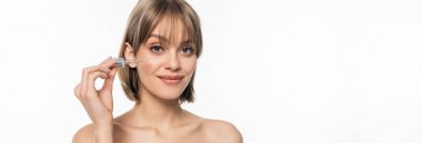 Beyaz pankarta izole edilmiş serumu kullanan kâküllü genç bir kadın.