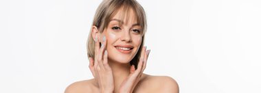 happy woman with bangs applying cream on cheeks and looking at camera isolated on white, banner