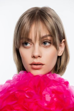 young woman with bangs looking away near bright pink decorative flower isolated on white