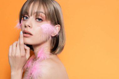 Makyajlı süs boncukları ve turuncu üzerinde pembe tüyleri olan genç bir kadın.