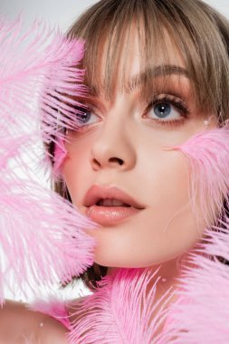close up of pretty woman holding pink feathers isolated on white