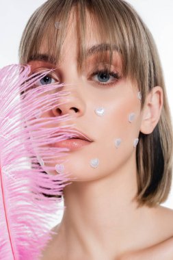 young woman with nacreous heart shape elements in makeup near pink feather isolated on white 