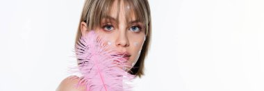 pretty woman with nacreous heart shape elements in makeup near pink feather isolated on white, banner