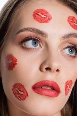 close up view of young woman with red kiss prints on cheeks looking away isolated on white
