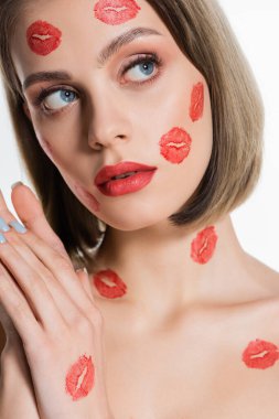 young woman with red kiss prints on cheeks and neck looking away isolated on white