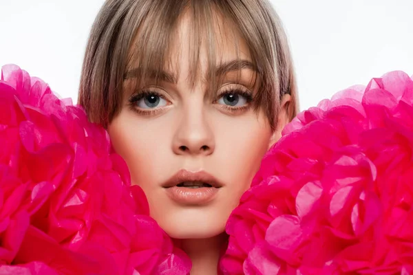 young woman with bangs near bright pink decorative flowers isolated on white