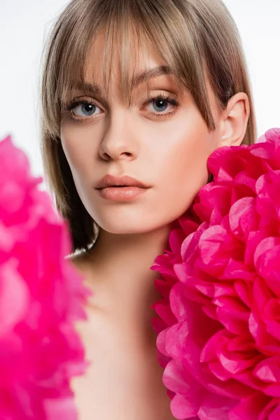 Parlak pembe çiçeklerin yanında kakülleri olan genç bir kadın beyaz üzerine izole edilmiş.