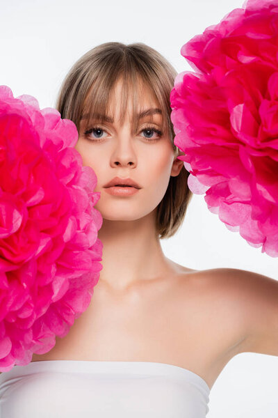 blonde young woman with bare shoulder looking at camera near bright pink flowers isolated on white