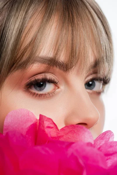 close up view of young woman with bangs looking at camera near bright pink flower isolated on white