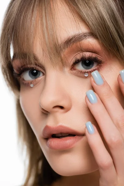 close up of woman with bangs applying shiny rhinestones under blue eyes isolated on white