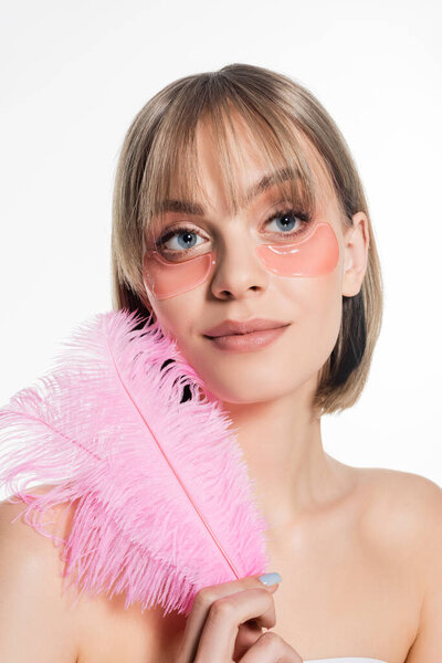 pleased young woman with hydrogel eye patches holding pink feather isolated on white