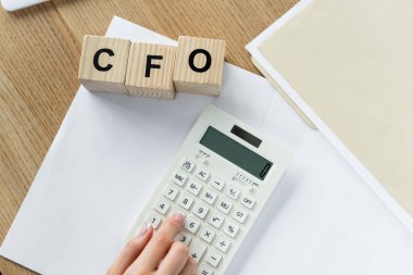 top view of chief financial officer using calculator near cubes with cfo lettering  clipart
