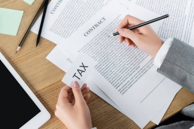 Vergi müfettişinin elinde kağıt tutarken dijital tabletin yanındaki sözleşmeyi kontrol ettiği görüntüler.