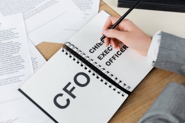 Not defterinin yanında elinde kalem olan CFO ve baş yönetici harfleri olan bir kadın görüntüsü. 