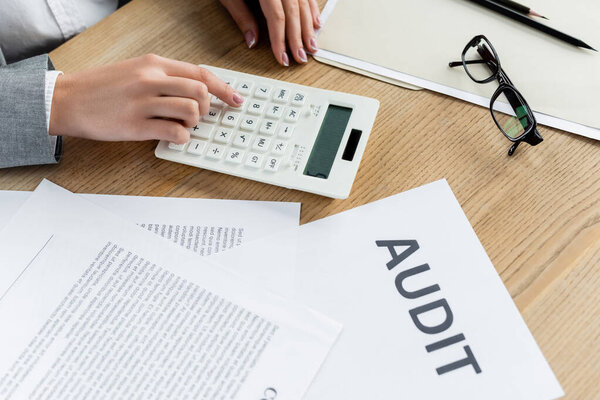 cropped view of tax inspector using calculator near paper with audit lettering 