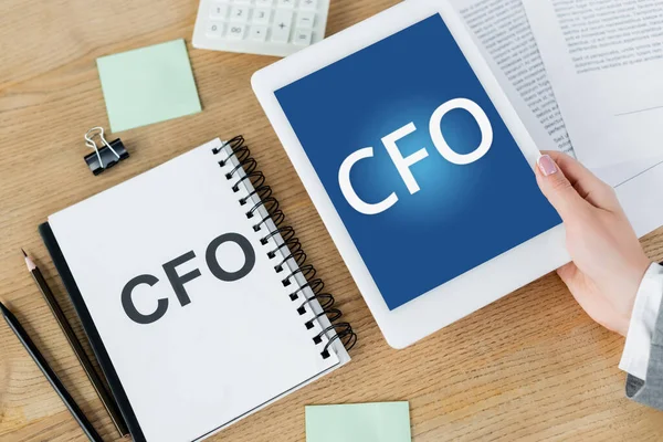 Not defteri ve kırtasiyenin yanındaki ekranda Cfo harfleriyle dijital tableti tutan kadının üst görünümü
