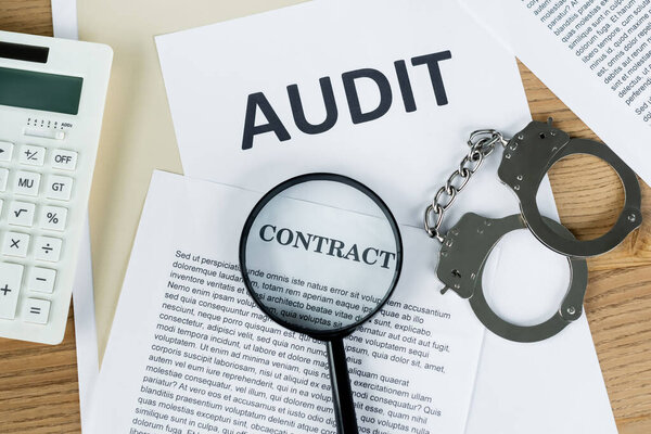 top view of magnifier on papers with audit and contract lettering near calculator and handcuffs 