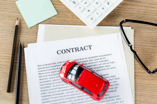 top view of toy car on contract near glasses, calculator and stationery