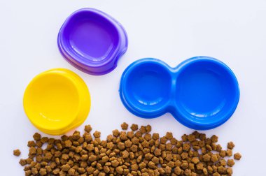 Beyaz üzerine izole edilmiş evcil hayvan mamasının yanındaki renkli plastik kaselerin üst görüntüsü
