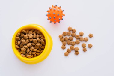 top view of dry and crunchy pet food near bowl and rubber toy isolated on white clipart