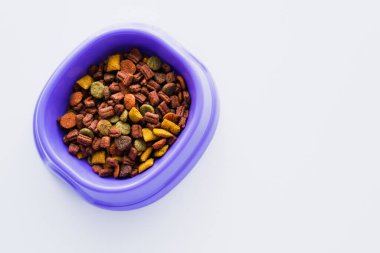 Beyaz üzerinde kuru köpek maması olan mor plastik kasenin üst görüntüsü.