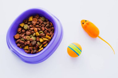 top view of purple plastic bowl with dry pet food near rubber toy mouse and ball isolated on white clipart