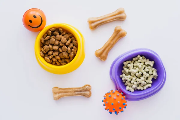 白色碗中干燥的宠物食品和橡胶玩具中骨头形宠物饼干的俯瞰图 — 图库照片