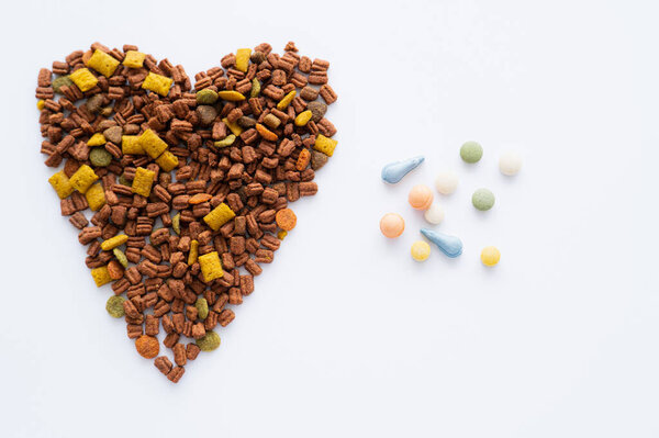 top view of heart made of crunchy dry pet food near vitamins in pills isolated on white