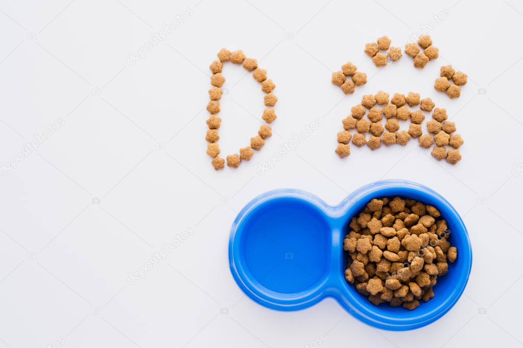 Top view of paw shape made of dry pet food near letter and bowls isolated on white