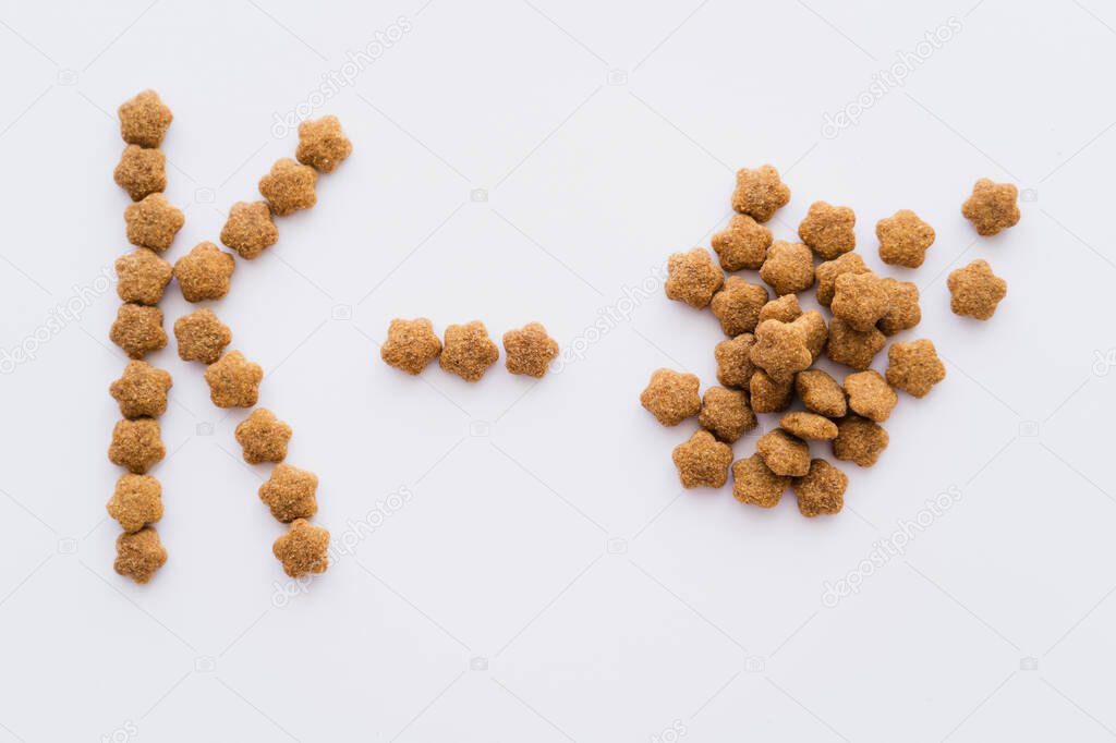 Top view of dry pet food near letter k isolated on white